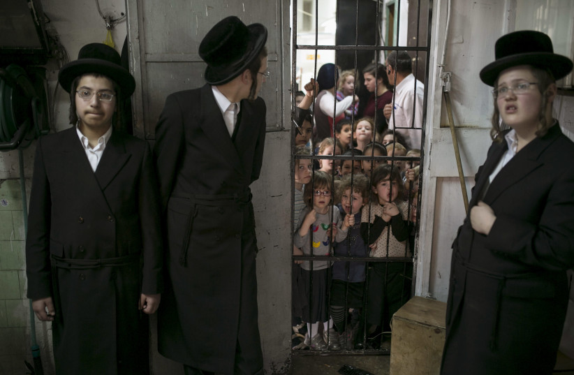 Schoolchildren stand in the doorway and watch as ultra-Orthodox Jews prepare matza in Bnei Brak near Tel Aviv March 30, 2015. (photo credit: BAZ RATNER/REUTERS)