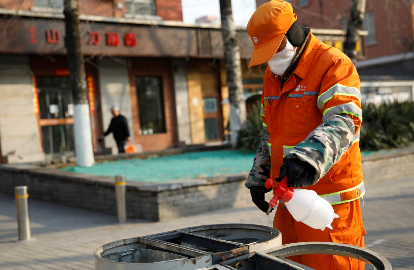 A street cleaner wearing a face mask sanitizes trash cans at a sidewalk, as the country is hit by an outbreak of the new coronavirus, in Beijing, China (photo credit: REUTERS/CARLOS GARCIA RAWLINS)