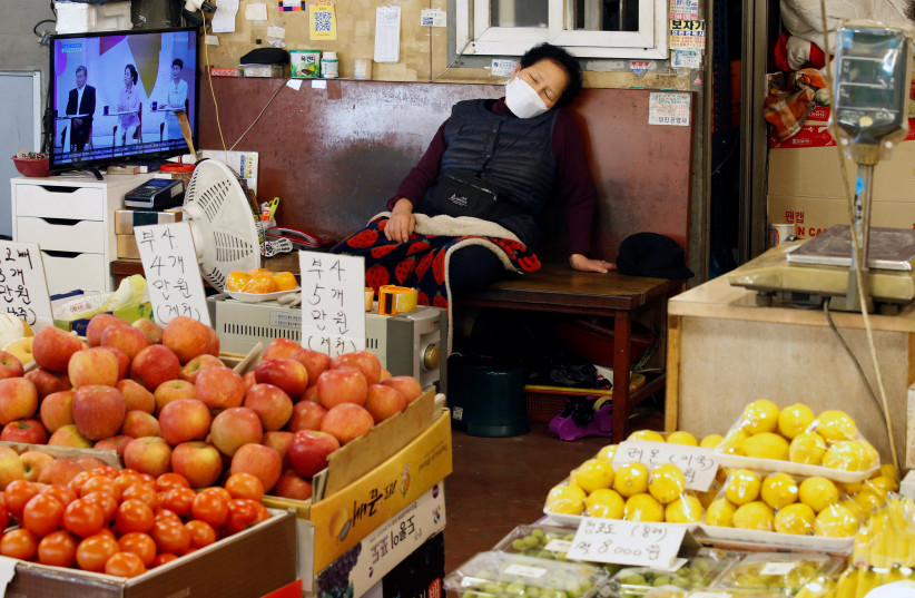A shopkeeper wearing a mask to prevent contracting the coronavirus takes a nap at a traditional market in Seoul (photo credit: REUTERS)