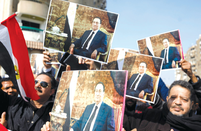 SUPPORTERS OF former Egyptian president Hosni Mubarak hold his photos near the main gate of a cemetery during his funeral ceremony, east of Cairo. (photo credit: REUTERS)