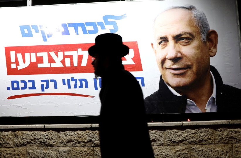 An ultra-Orthodox Jewish man walks past a Likud election campaign poster depicting Israeli Prime Minister Benjamin Netanyahu, in Jerusalem February 25, 2020 (photo credit: AMMAR AWAD / REUTERS)
