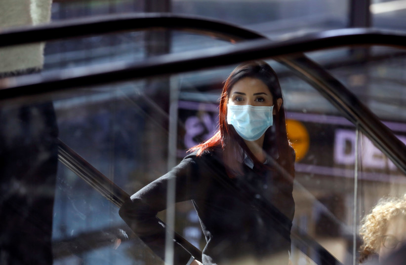 A woman wearing a mask looks on at a terminal at Ben Gurion International airport in Lod, near Tel Aviv, Israel (photo credit: REUTERS/AMIR COHEN)