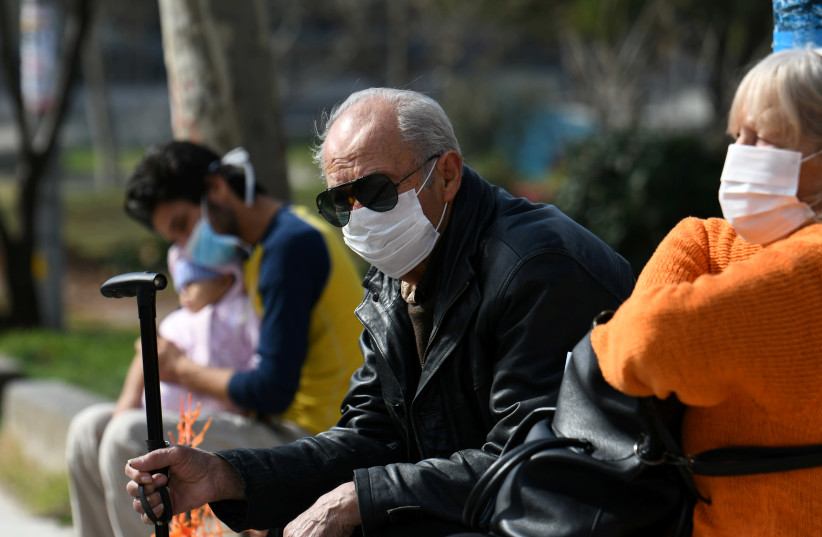 People wearing protective face masks sit outside the AHEPA hospital, where the first confirmed coronavirus case is being treated, in Thessaloniki, Greece, February 26, 2020 (photo credit: ALEXANDROS AVRAMIDIS/REUTERS)