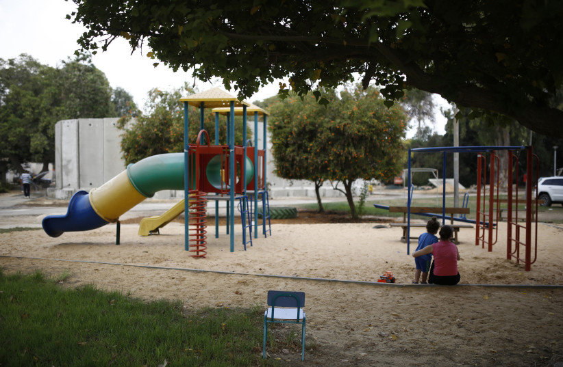 An Israeli woman and a child sit at a playground near a kindergarten surrounded by concrete blast walls on the first day of the school year in Nahal Oz (photo credit: AMIR COHEN)
