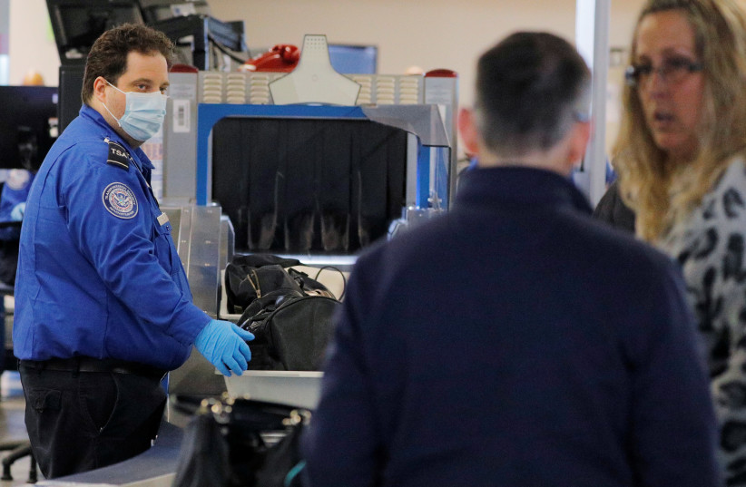A TSA officer wears a mask and gloves, amid the worldwide coronavirus outbreak, at Logan International Airport in Boston, Massachusetts, U.S., March 11, 2020 (photo credit: REUTERS/BRIAN SNYDER)