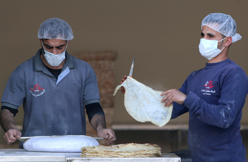 Palestinian workers, wearing masks amid coronavirus precautions, bake bread at a bakery in Gaza City March 8, 2020 (photo credit: REUTERS/MOHAMMED SALEM)