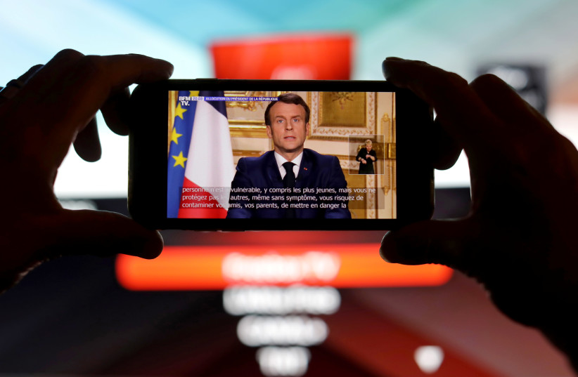 French President Emmanuel Macron is seen addresses the nation about the coronavirus disease (COVID-19) outbreak, on a mobile screen in this illustration picture (photo credit: REUTERS)