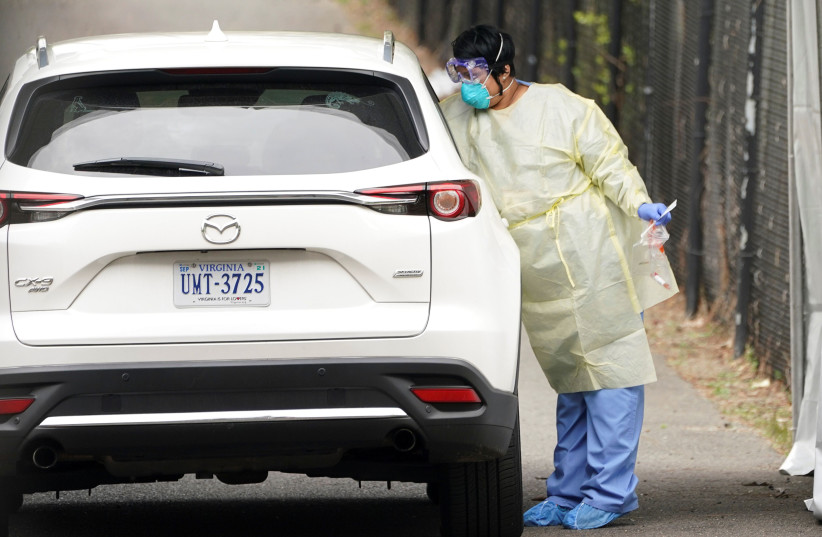 A healthcare worker reaches in to takes a swab from a passenger at a drive-through site to collect samples for coronavirus testing in Arlington, Virginia, U.S., March 18, 2020 (photo credit: REUTERS/KEVIN LAMARQUE)