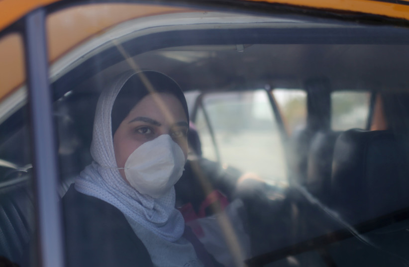 A Palestinian woman, wearing a mask as a preventive measure against coronavirus, looks out of a car upon her return from abroad, at Rafah border crossing in the southern Gaza Strip (photo credit: REUTERS)