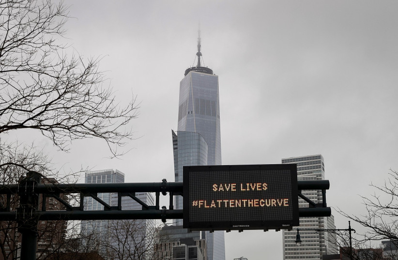 One World Trade is seen behind a sign that flashes an emergency alert, as the coronavirus disease (COVID-19) outbreak continues in New York City, New York, U.S., March 23, 2020 (photo credit: REUTERS/MIKE SEGAR)