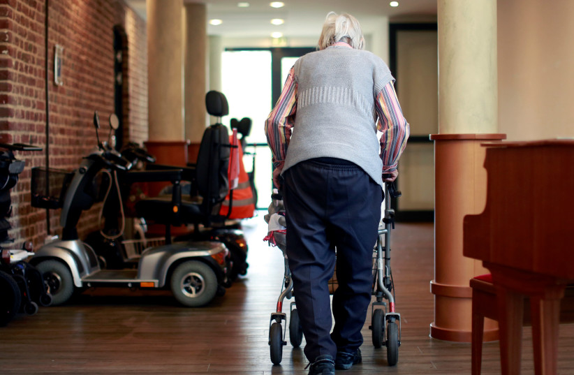 An elderly woman walks through a corridor of a retirement home as visits have been restricted due to the coronavirus disease (COVID-19) concerns, in Grevenbroich (photo credit: REUTERS)