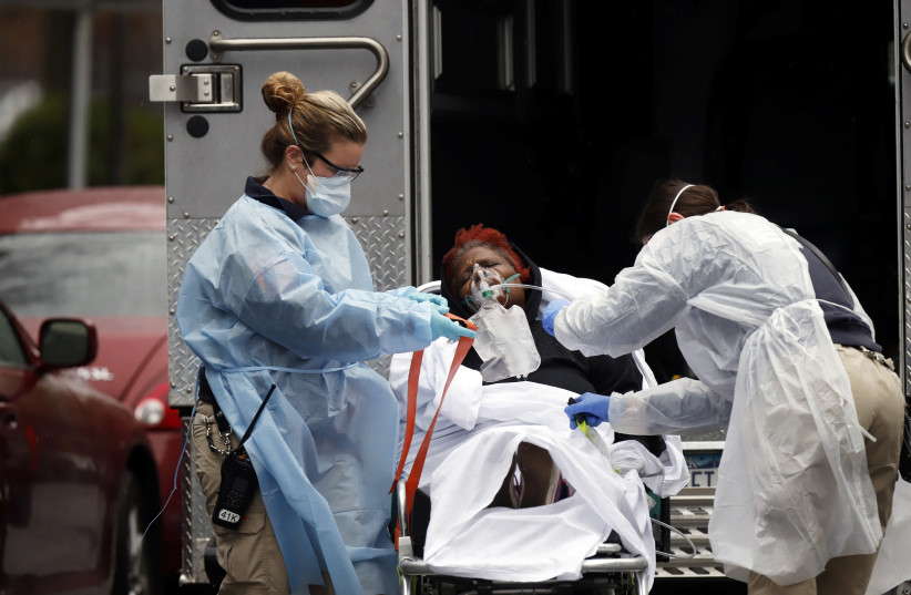 Emergency Medical Technicians wearing protective gear wheel a sick patient to a waiting ambulance during the outbreak of coronavirus disease in New York City, March 28, 2020 (photo credit: REUTERS/STEFAN JEREMIAH)