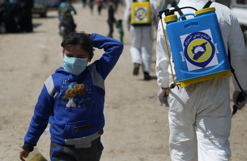 An internally displaced Syrian girl wears a face mask as members of the Syrian Civil defence sanitize the Bab Al-Nour internally displaced persons camp, to prevent the spread of coronavirus disease (COVID-19) in Azaz, Syria March 26, 2020 (photo credit: KHALIL ASHAWI / REUTERS)