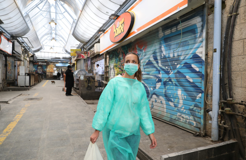 A woman in protective gear from coronavirus walks through Mahane Yehuda market (photo credit: MARC ISRAEL SELLEM)