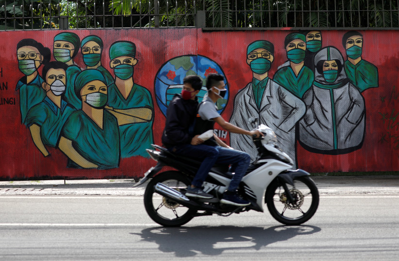 Men wearing face masks ride past a mural showing a thank you to country's medical workers tackling coronavirus disease (COVID-19) amid its spread, at a road in Depok, south of Jakarta, Indonesia, April 7, 2020 (photo credit: REUTERS/WILLY KURNIAWAN)