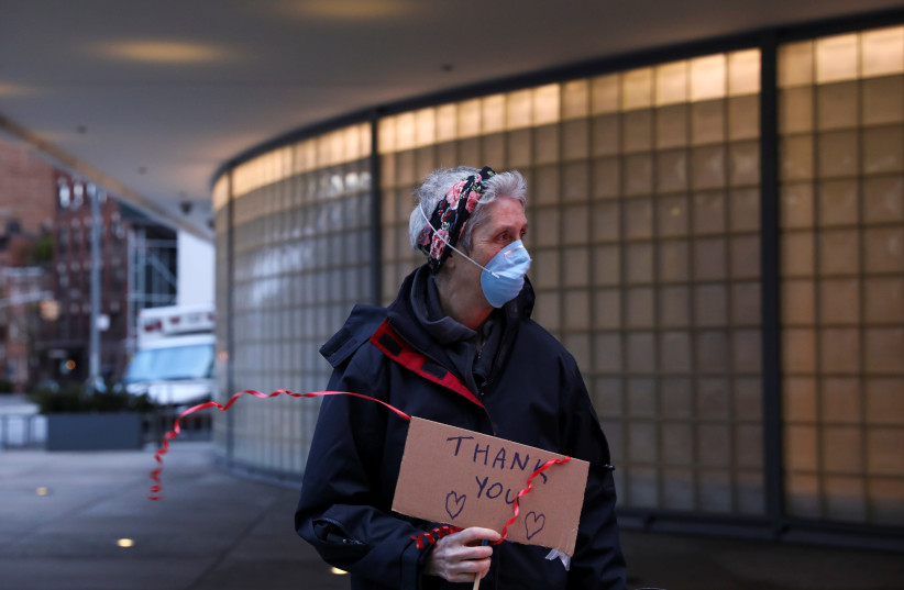 A woman holds a sign to thank medical workers outside the Phyllis And William Mack Pavilion during the outbreak of the coronavirus disease (COVID-19) in the Manhattan borough of New York City, New York, U.S., April 10, 2020 (photo credit: REUTERS/CAITLIN OCHS)