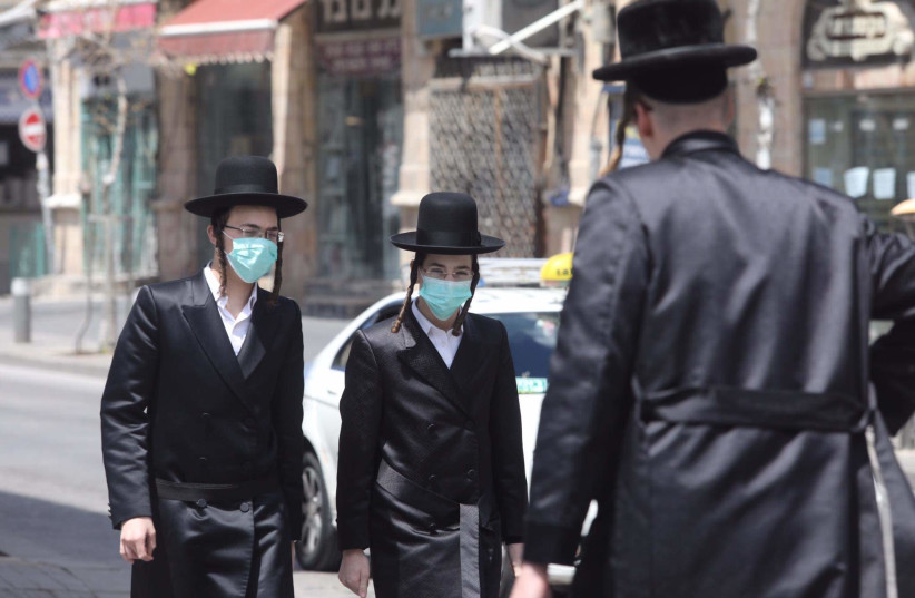 Ultra-Orthodox men wearing masks walk around the neighborhood of Mea Shearim, Jerusalem, April 12, 2020  (photo credit: MARC ISRAEL SELLEM/THE JERUSALEM POST)