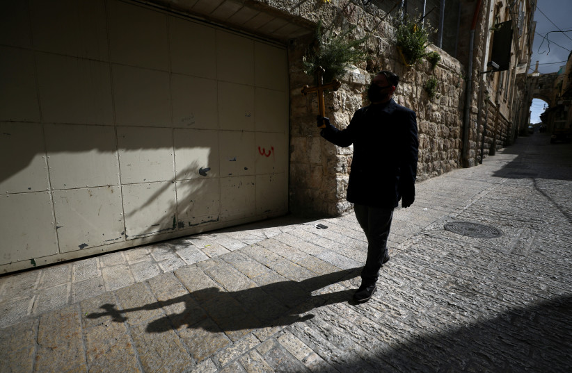 A worshipper holds a cross in Jerusalem's Old City on the day that Greek Orthodox church authorities celebrate Good Friday amid the coronavirus disease (COVID-19) outbreak, in Jerusalem April 17, 2020. (photo credit: AMMAR AWAD/REUTERS)