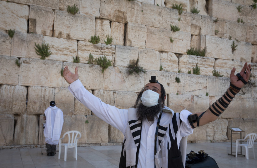 Jewish men pray at the Western Wall, Judaism's holiest prayer site, in Jerusalem's Old City. April 19, 2020. (photo credit: NATI SHOCHAT/FLASH 90)