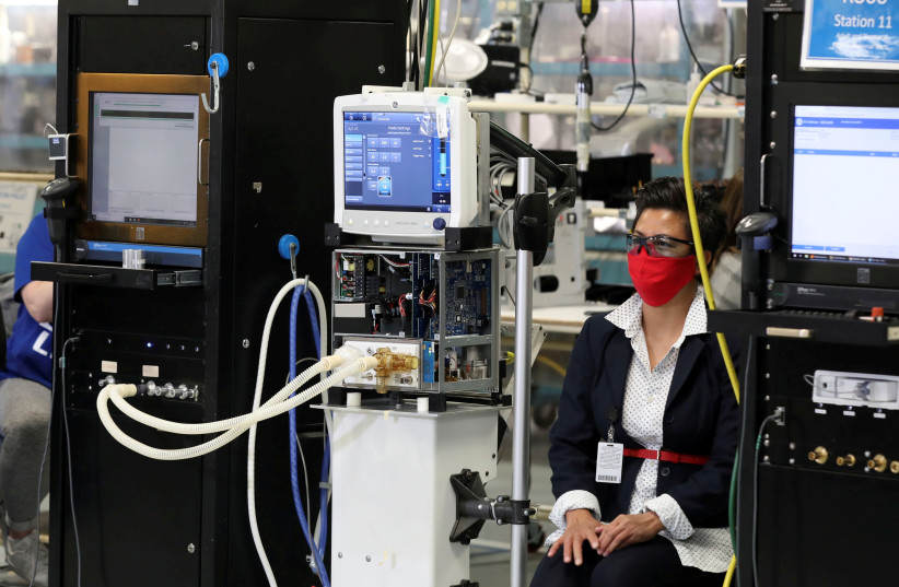 An employee wearing a face mask sits next to a GE Carescape R860 ventilator in an assembly and testing area at a GE Healthcare manufacturing facility during the global coronavirus disease (COVID-19) outbreak in Madison, Wisconsin, U.S. April 21, 2020 (photo credit: REUTERS)