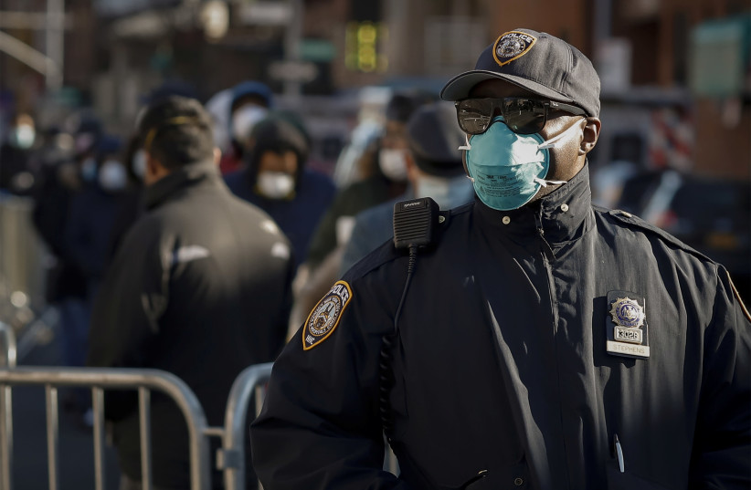 A New York City Police officer (NYPD) wears protective gear, while monitoring people waiting in line to be tested for coronavirus disease (COVID-19). March 26, 2020. (photo credit: REUTERS/STEFAN JEREMIAH)