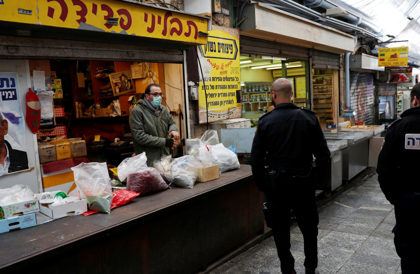 Israeli policemen walk past a vendor sorting through items before closing his shop at a market in Jerusalem (photo credit: RONEN ZVULUN/REUTERS)