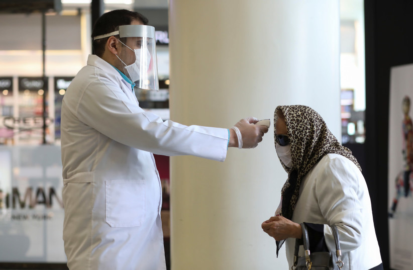 A man wears a face mask and a protective face shield as he checks a woman's temperature, to let her go inside the mall, following the outbreak of the coronavirus disease (COVID-19), after shopping malls and bazaars reopened in Tehran, Iran, April 20, 2020 (photo credit: WANA (WEST ASIA NEWS AGENCY)/ALI KHARA VIA REUTERS)