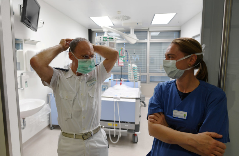 Anesthesiologists Matthias Helm and Sylvie Thierbach of the German armed forces Bundeswehr stand in front of a room in the intensive care unit of the Ulm Bundeswehr hospital as they prepare for the admission of patients, while the spread of the coronavirus disease (COVID-19) continues, in Ulm, Germa (photo credit: ANDREAS GEBERT/REUTERS)