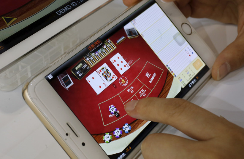An attendant demonstrates an online baccarat game on a smartphone at the Global Gaming Expo (G2E) Asia in Macau, China (photo credit: BOBBY YIP/ REUTERS)