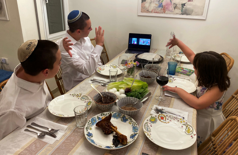 Three siblings in Mevaseret Zion, near Jerusalem, wave to their their grandmother in Haifa as she joins their Passover Seder via Zoom  (photo credit: REUTERS/DAN WILLIAMS)