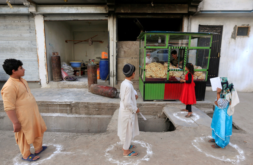 Afghan youths stand on social distancing markers as they buy bread from a bakery, amid the spread of the coronavirus disease (COVID-19), in Jalalabad, Afghanistan May 8, 2020. (photo credit: REUTERS/PARWIZ)