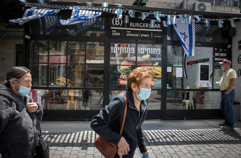 Israelis wearing face masks and gloves, walk outside an open restaurant proposing take aways and deliveries  takes away on May 06, 2020 in Jerusalem. (photo credit: OLIVIER FITOUSSI/FLASH90)