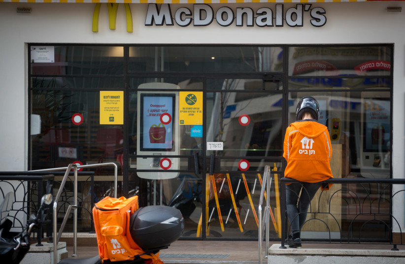 A food delivery man waits outside a McDonalds restaurant in Tel Aviv. April 18, 2020 (photo credit: MIRIAM ALSTER/FLASH90)