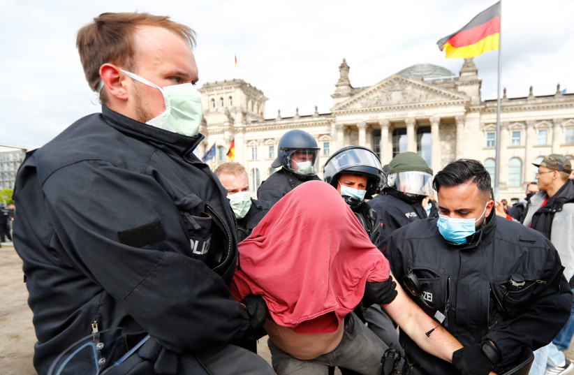Police officers wearing protective face masks detain a demonstrator during a protest against the government's restrictions following the coronavirus disease (COVID-19) outbreak, in front of Reichstag, in Berlin, Germany May 16, 2020.  (photo credit: REUTERS/FABRIZIO BENSCH)
