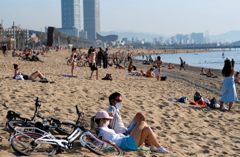A couple wearing face masks enjoy the sunny weather at Barceloneta beach, amid the coronavirus disease (COVID-19) outbreak, in Barcelona, Spain, May 22, 2020 (photo credit: REUTERS/NACHO DOCE)