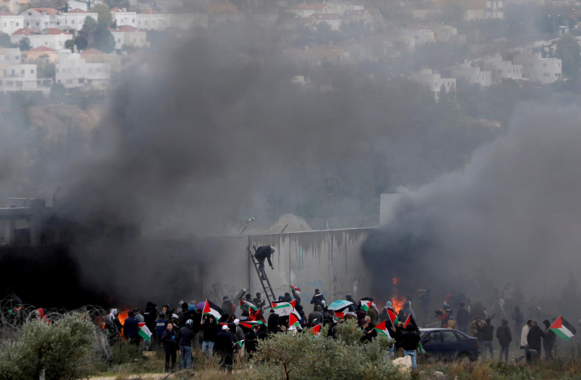 Palestinian demonstrators protest by the separation barrier, with Modiin Illit in the background. February 7, 2020 (photo credit: REUTERS/MOHAMAD TOROKMAN)