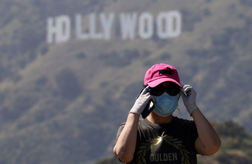 A person wearing a face mask and gloves adjusts glasses while taking photos of the Hollywood sign after a partial reopening of Los Angeles hiking trails during the outbreak of the coronavirus disease (COVID-19) at Griffith Park in Los Angeles, California, U.S., May 9, 2020 (credit: REUTERS)