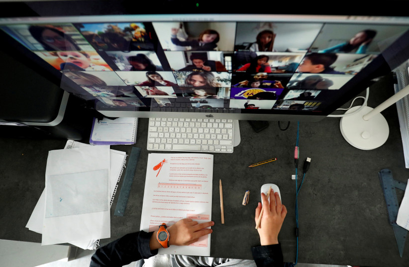 FILE PHOTO: A student takes classes online with his companions using the Zoom app at home (credit: REUTERS)