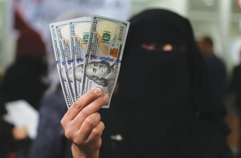 A HAMAS CIVIL servant in Gaza displays US dollar banknotes after receiving her salary paid by Qatar, in December 2018. (credit: IBRAHEEM ABU MUSTAFA/REUTERS)