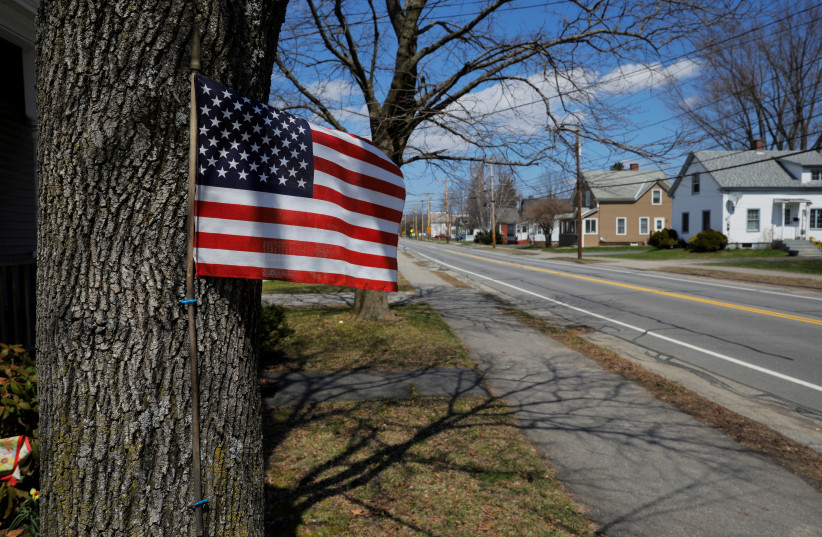 A U.S. flag hangs on a tree trunk amid the coronavirus disease (COVID-19) outbreak in Keene, New Hampshire, U.S., April 19, 2020. (photo credit: REUTERS/BRIAN SNYDER)