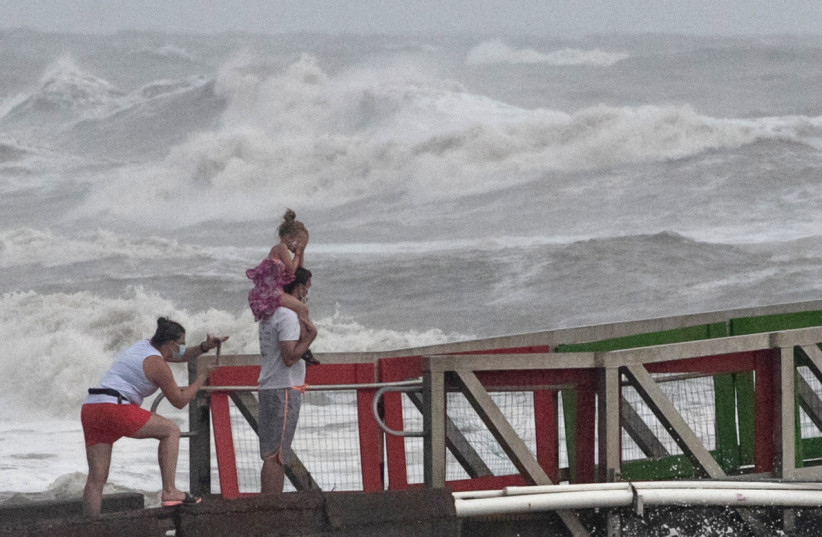 A girl covers her face from strong winds as her family members watch high swells from Hurricane Hanna from a jetty in Galveston, Texas, U.S., July 25, 2020. (credit: REUTERS/ADREES LATIF)
