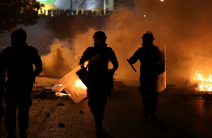 Lebanese riot police walk near burning fire during a protest against the fall in pound currency and mounting economic hardship, in Beirut, Lebanon (photo credit: REUTERS/MOHAMED AZAKIR)