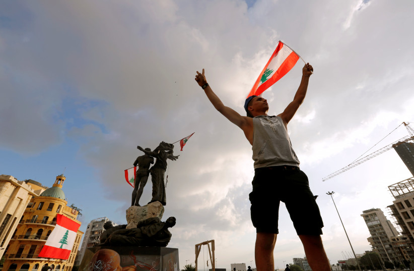A demonstrator holds the Lebanese flag in Martyrs' Square where protests are held following Tuesday's blast in Beirut, Lebanon August 9, 2020 (photo credit: REUTERS/THAIER AL-SUDANI)