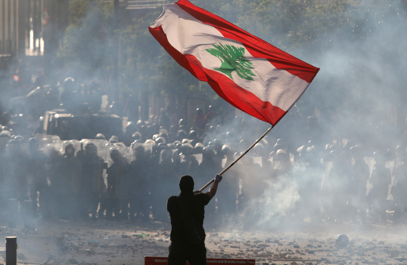 A demonstrator waves the Lebanese flag in front of riot police during a protest in Beirut, Lebanon, August 8, 2020 (credit: GORAN TOMASEVIC/REUTERS)