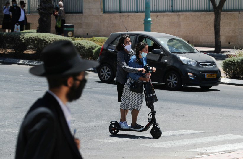 Israeli youths wearing masks ride a scooter as Israeli authorities brought back some coronavirus disease (COVID-19) restrictions after the number of new cases jumped in what officials fear could herald a "second wave" of infections, in Elad, Israel June 24, 2020 (photo credit: REUTERS/AMMAR AWAD)