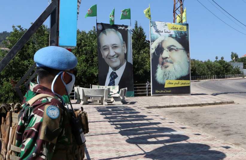 A United Nations peacekeeper (UNIFIL) stands near a poster depicting Lebanon's Hezbollah leader Sayyed Hassan Nasrallah, in Adaisseh village, near the Lebanese-Israeli border, Lebanon August 7, 2020. (photo credit: REUTERS/KARAMALLAH DAHER)