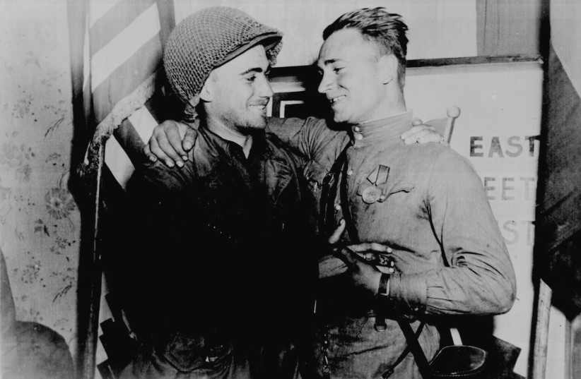 SOVIET LT. Alexander Sylvashko and US 2nd Lt. William Robertson stand in front of a sign symbolizing the historic meeting of the Russian and American armies near Torgau, Germany, on April 25, 1945. (photo credit: US NATIONAL ARCHIVES/REUTERS)