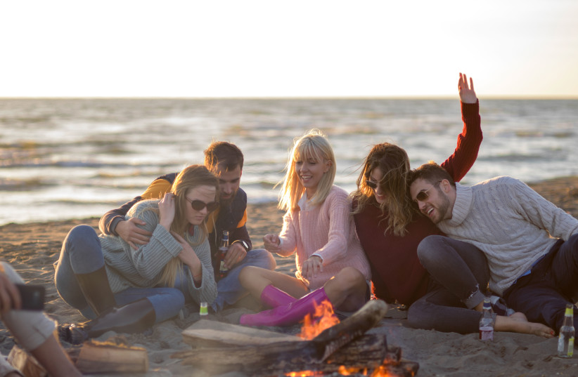 Friends drinking by a campfire on a beach (Illustrative) (photo credit: INGIMAGE)