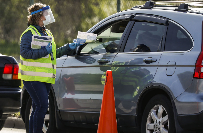  health care worker hands out testing information to people waiting at a drive-through COVID-19 testing site in Chicago, May 6, 2020 (photo credit: JOEL LERNER/XINHUA VIA GETTY/JTA)