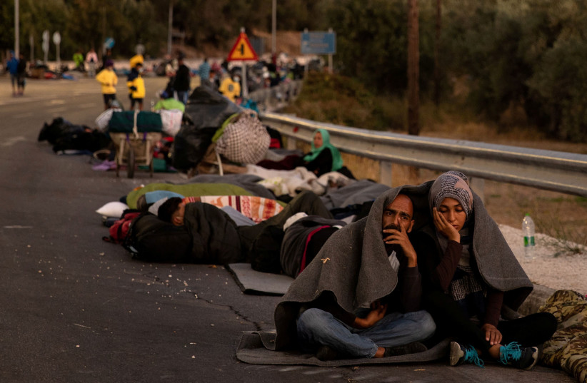 Couple sits covered with a blanket as refugees and migrants camp on a road following a fire at the Moria camp on the island of Lesbos (photo credit: REUTERS)